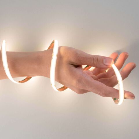 ein warmweiß leuchtender COB LED Streifen mit flexibler Leiterplatte leuchtet und ist um eine weibliche Hand geschlungen