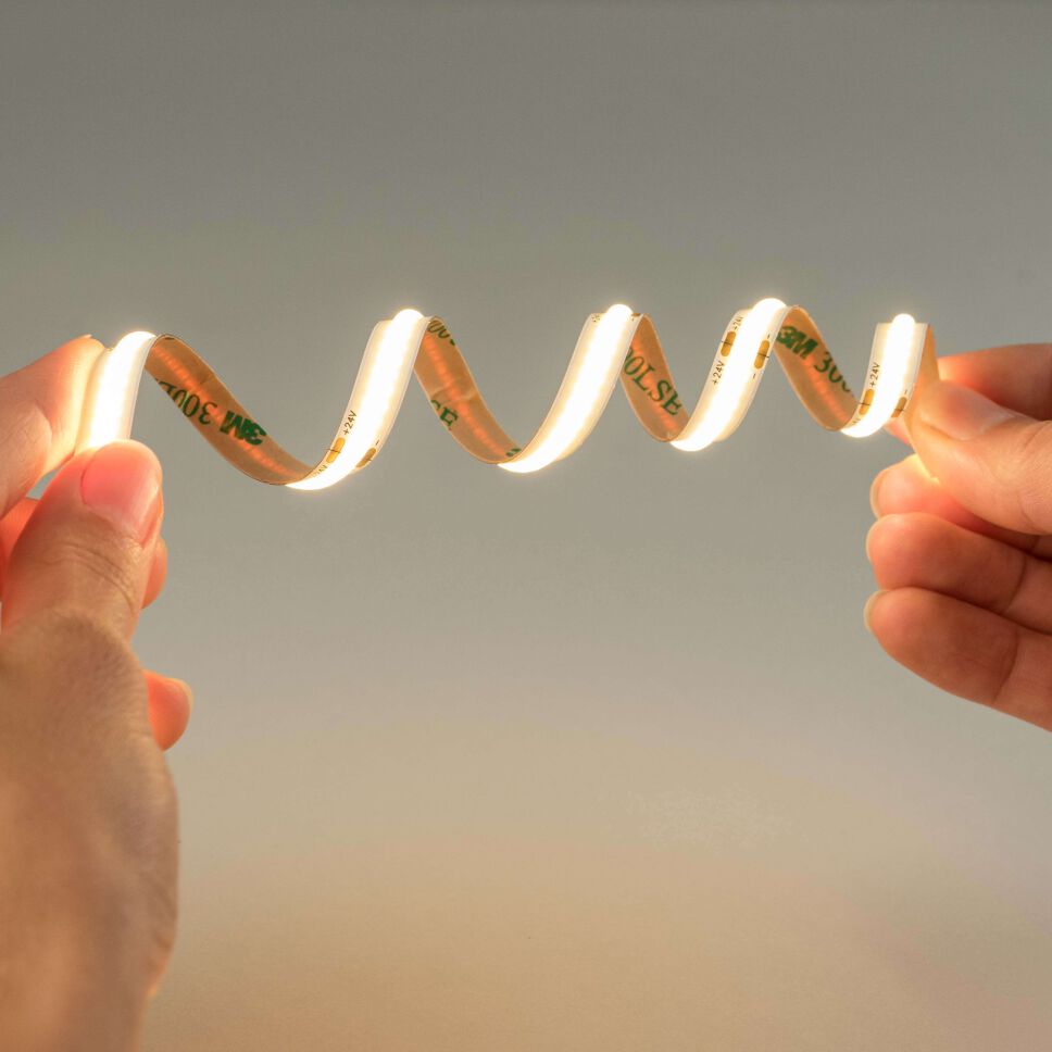 2 Hände halten einen warmweiß leuchtenden und verdrehten COB LED Streifen mit flexibler Leiterplatte